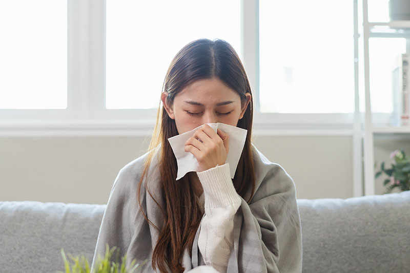 Young woman with a common cold sneezing on a sofa at home.