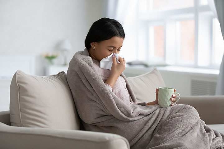 Sick woman wrapped in a blanket blows her nose.